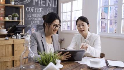 Two confident asian japanese female businesspeople using digital tablet together while working at...