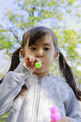 緑の中でシャボン玉で遊ぶ幼児(5歳児)