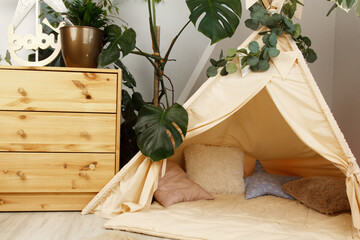 interior of a children's room or recreation area: a wigwam with soft pillows, a wooden nightstand made of environmentally friendly materials. plastic plants to decorate the space © skeronov