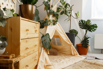 interior of a children's room or recreation area: a wigwam with soft pillows, a wooden nightstand made of environmentally friendly materials. plastic plants to decorate the space © skeronov