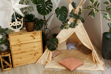interior of a children's room or recreation area: a wigwam with soft pillows, a wooden nightstand made of environmentally friendly materials. plastic plants to decorate the space © skeronov