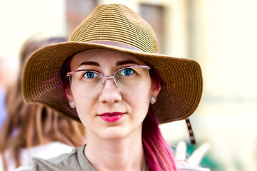 A young hipster woman looks into the camera, beautiful face, expressive eyes, posing in an urban area on an autumn day, outdoors, stylish hat and transparent glasses. The concept of happy people.