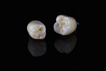two dental crowns with tooth morphology on a black background with reflection