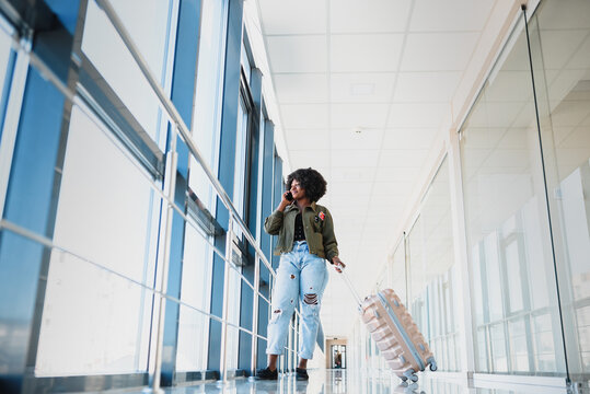 Full Length Side Portrait Of Young Black Woman Walking With Suitcase In Airport