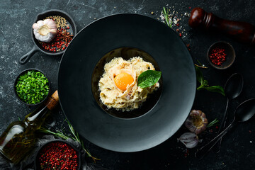 Carbonara pasta with egg and parmesan cheese and basil in a plate on a black stone background. Top view. Rustic style.