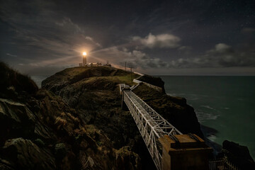South Stack Lighthouse near Holyhead Anglesey in North Wales, at night with stars and light beams...