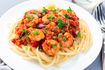 Italian dish shrimp linguine Puttanesca, pasta with shrimps in spicy tomato basil sauce garnished with parsley, horizontal, closeup