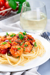 Italian dish shrimp linguine Puttanesca, pasta with shrimps in spicy tomato basil sauce garnished with parsley, vertical