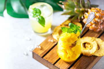 Homemade pineapple sorbet ice cream in a glass on a wooden background.
