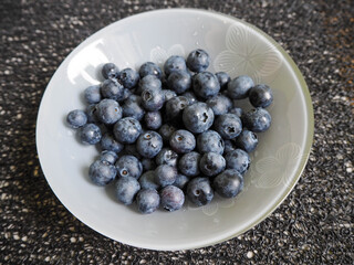 a grey glass round plate with blue blueberries on a dark structural table top view . blue berries