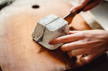 Valencay cheese on a wooden board. Cheesemaker cuts cheese with blue mold, close-up. French soft cheese from goat's milk. Cheese composition. Copy Space. Place for text.