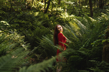 The young woman in red dress in rainforest with fern. Concept of nature and happy life, adventure. Beautiful light.