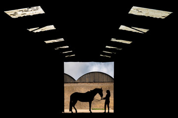 Silhouette of a horse and rider in the entrance of a farm yard barn