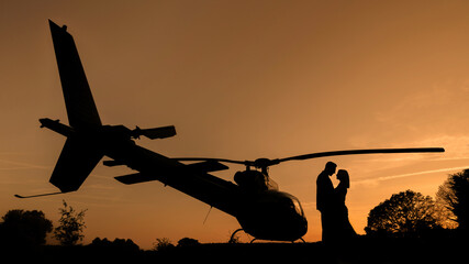 Bride and groom wedding day sunset silhouette with a Helicopter against an orange sky. © Chris Chambers