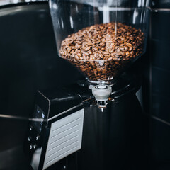 Coffee beans in an electric commercial coffee grinder in a cafe - professional barista