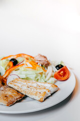 Sea bass fish steak golden grilled with fresh salad on white plate and white background