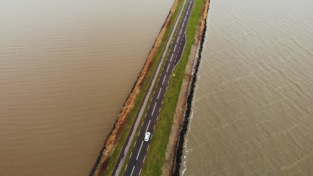 Aerial Top View shot of White car moving by the Highway Road on the Dam in Netherlands connecting Mainland with a Marken island in Holland
