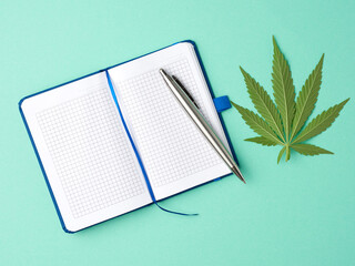 open notebook and green leaf of hemp on a light green background