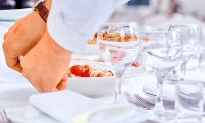 waiter by catering is preparing a table for party. Closeup hands. Glasses, plates, delicious 