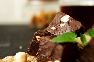 Fondant on craft crumpled paper with nuts and chocolate cubes decorated with green mint leaves. In the background a jar of nuts, blurred background. 