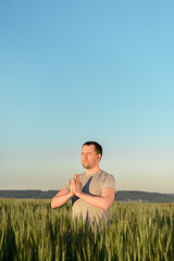 Adult man stands on a field in tall grass doing yoga during sunset. Digital detox, connection with nature concept. Copy space, vertical.