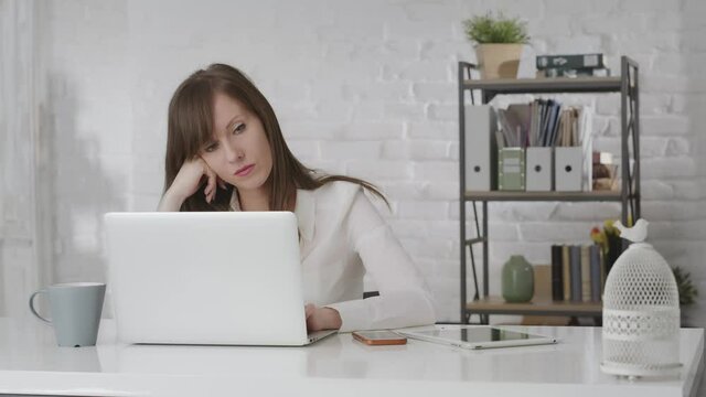 Woman working at office desk with laptop computer, looking bored, getting a pile of documents and new work from boss.