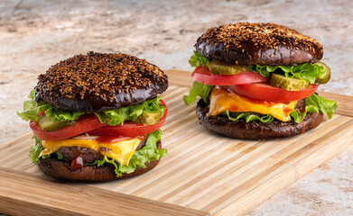 classic american homemade burger on the kitchen board. Bun with sesame seeds, pickled cucumbers, cheddar cheese, tomatoes, onions, meat cutlet.