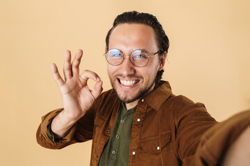 Image of happy man in eyeglasses gesturing ok sign while taking selfie photo