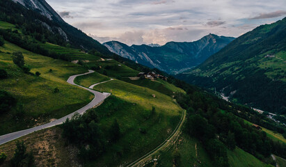 Fototapeta na wymiar Aerial view of picturesque valley in area of wild green Swiss hills. Bird's eye view of breathtaking countryside in mountains. Beautiful bicycle path spreads in hills of stunning nature landscape