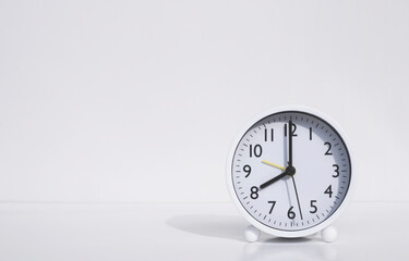 White round alarm clock in 8 o'clock on tabletop with white wall background