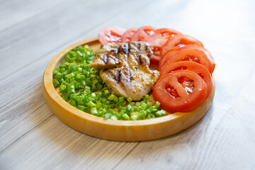 a piece of grilled pork with tomato and green onion on a wooden plate
