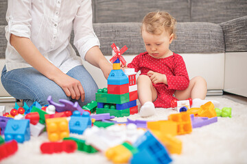 Child girl with mom play in multi-colored toy blocks and cubes.