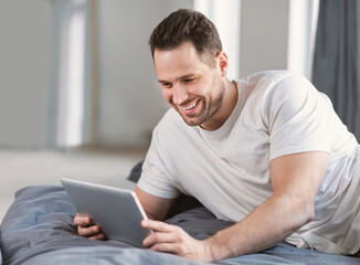 Man Using Digital Tablet Watching Movie Lying In Bed Indoors