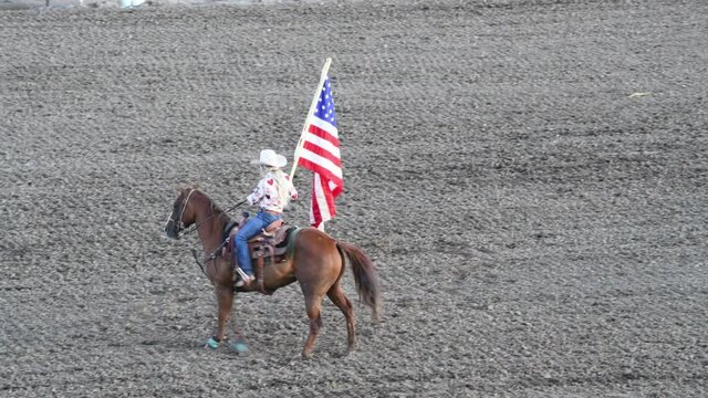 Girl with hat riding a horse ar rodeo park holding american flag