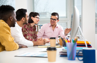 Multy-ethnic group of business people working while sitting at the office desk and smiling at camera