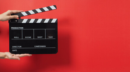 A Hand is holding Black clapper board or movie slate on red background.It used in cinema industry...