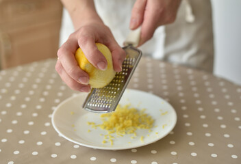 Closeup of woman rubbing lemon zest on grater