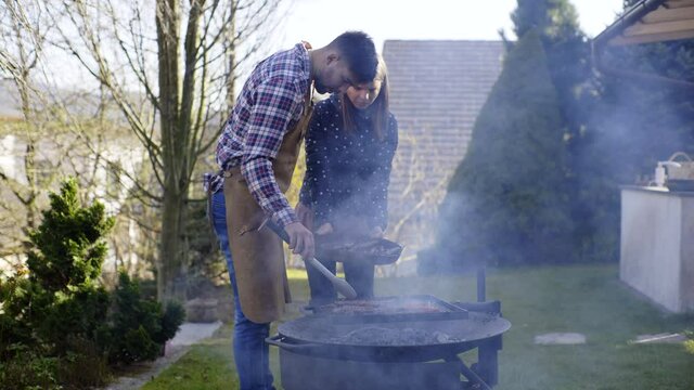 Man and woman collecting meat from the from the grill fire pit, smoke into camera