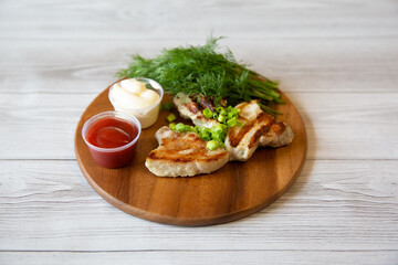 a piece of grilled pork with tomato sause and mayonnaise on a wooden plate