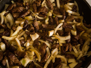 The meat with onions is fried in a pan. Beef stroganoff cooking. Close-up