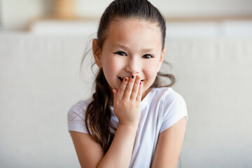 Fototapeta na wymiar Cute Girl Laughing Covering Mouth Sitting On Couch At Home