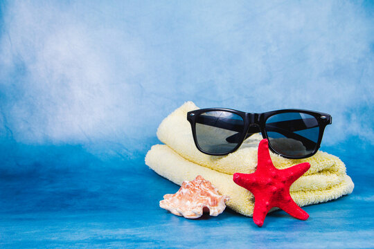 Sunglasses, towel, seashell and starfish on the blue background