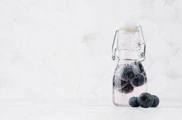 Fresh summer pink cocktail with ripe blueberry, soda, berry in yoke bottle on elegant soft light white wooden board and plaster wall.