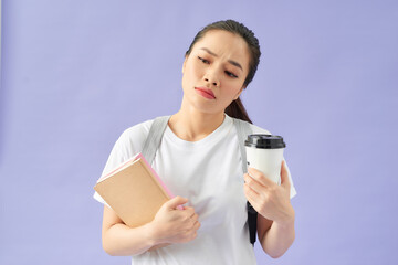 Displeased woman student wearing backpack on purple background. Hold books cup of coffee or tea