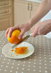 Closeup of woman rubbing orange zest on grater