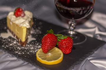 Piece of cake with chocolate and delicate lemon cream and strawberrys. A glass of red wine with strawberries and oranges shared with a loved one