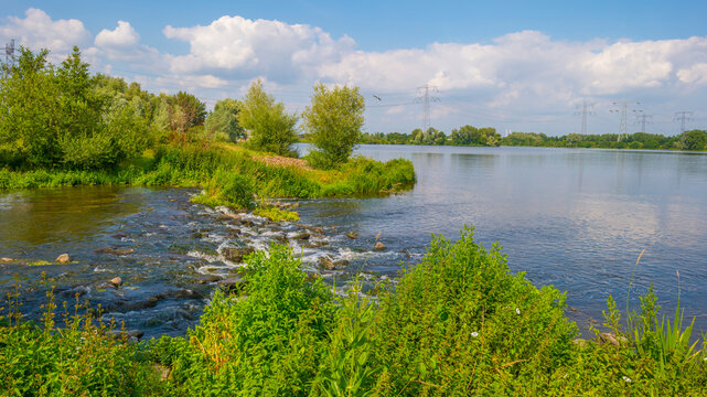 Stream with rapids along the grassy green edge of a lake below a blue sky in summer