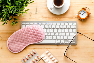 Sleeping on office desk. Concept with sleep mask and laptop top view on wooden
