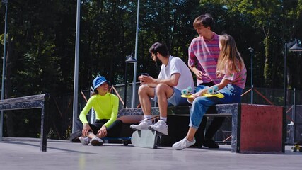 Beautiful ladies multiethnic and two smiling large guys meeting in a urban skate park they have a socializing time before start to ride on a skateboard wearing modern outfits - Powered by Adobe