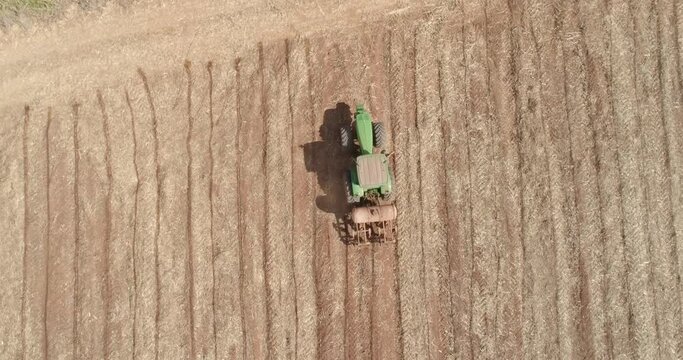 Aerial view of tractor with mounted seeder performing direct seeding of crops on plowed agricultural field. Farmer is using farming machinery for planting process, Brazilian farm. 4K.